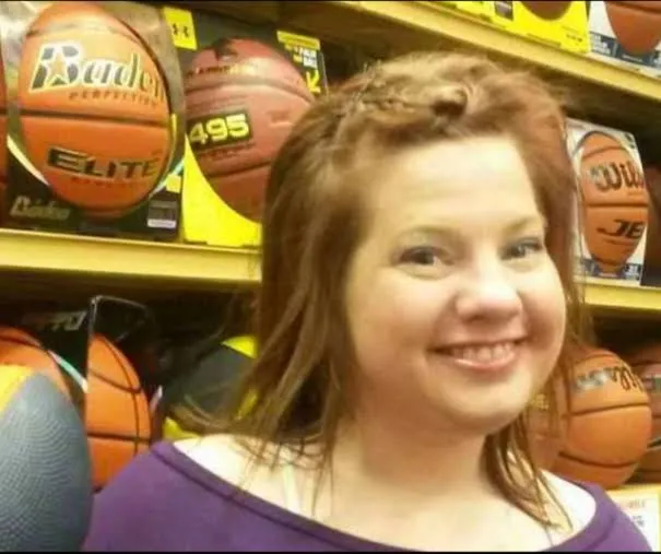 Alicia Hummel smiling, in a purple top, in front of store shelves stacked with basketballs