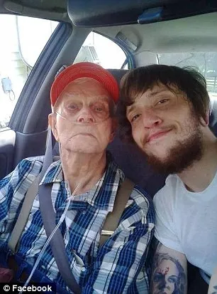 An older man in a red cap and plaid shirt, wearing an oxygen tube, beside a bearded young man in a car