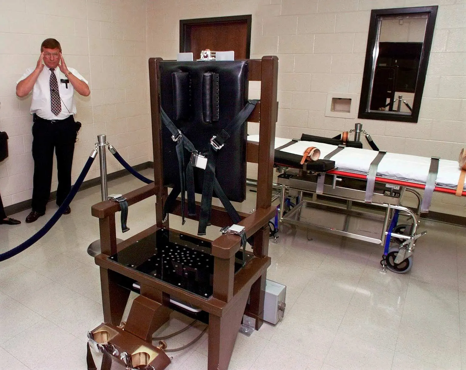An execution chamber with an electric chair in front and a lethal injection gurney behind it