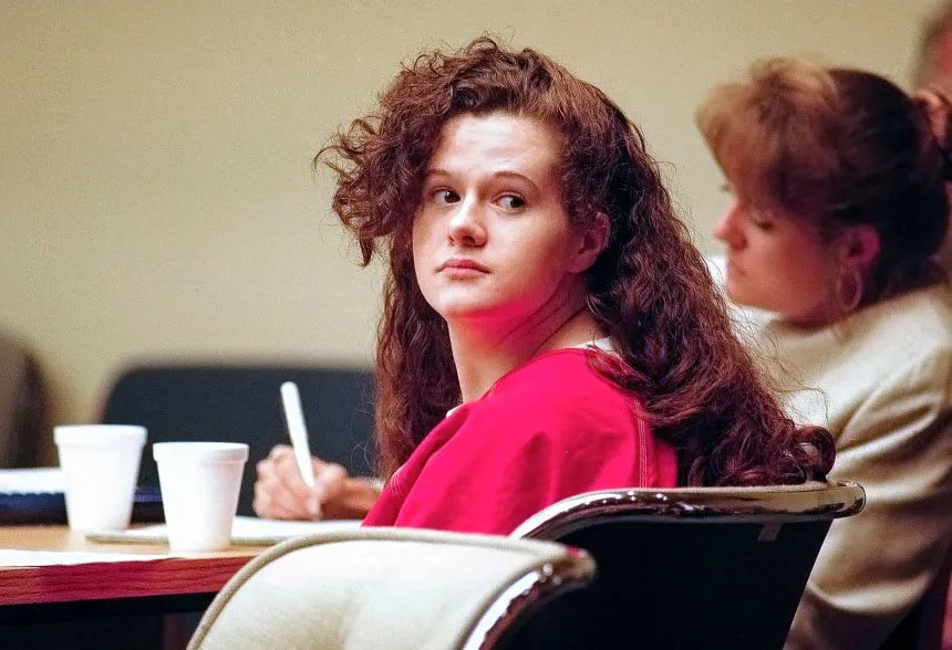 Christa Pike in a red jail uniform, looking over her shoulder from the defense table
