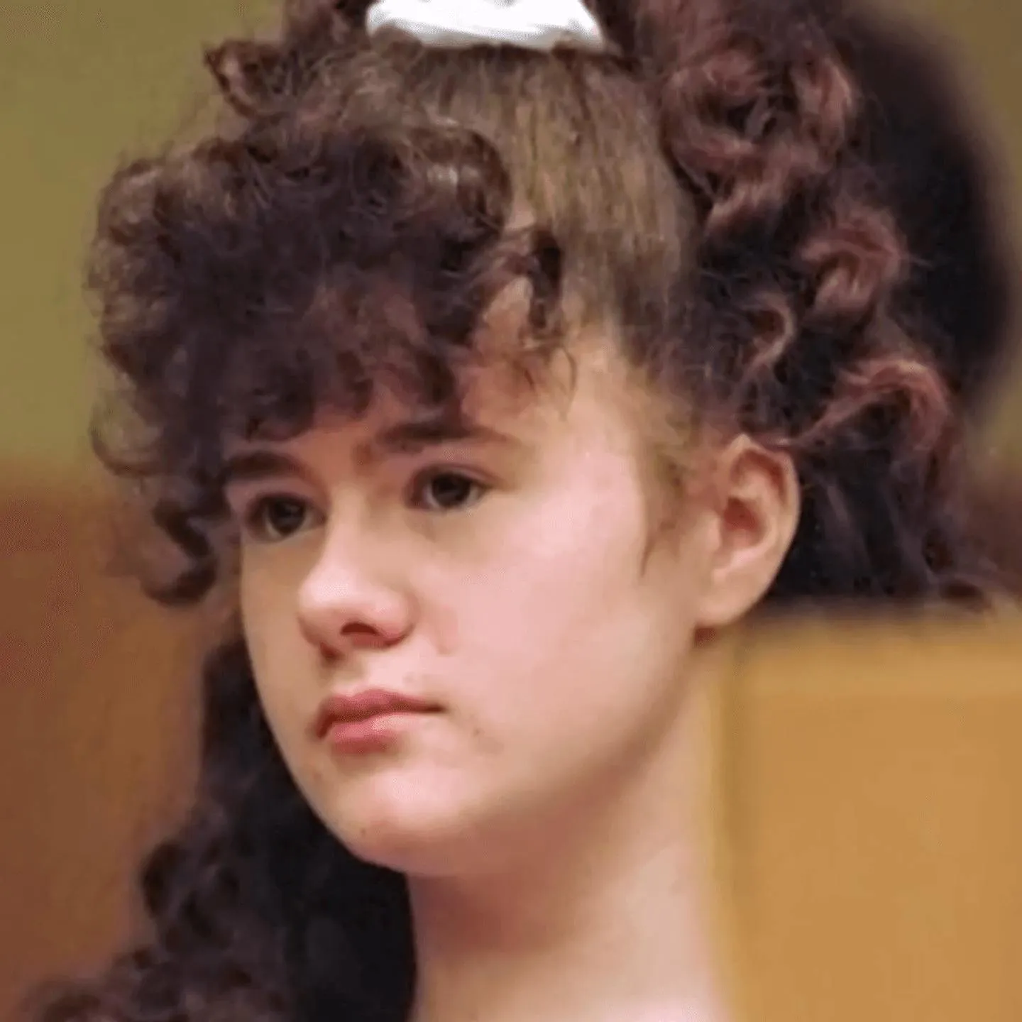 Christa Pike as a teenager with curly hair and a white bow, in a courtroom