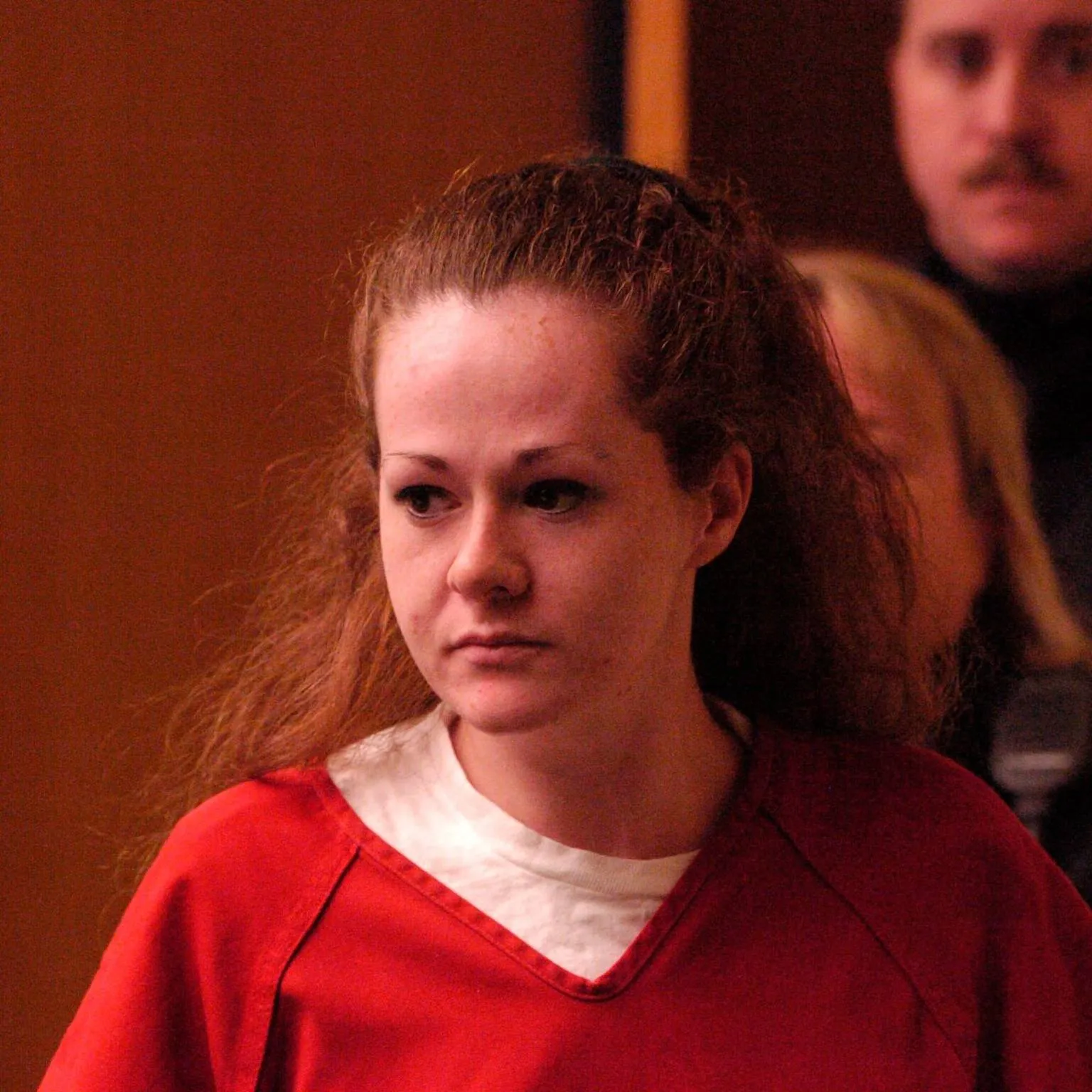 Christa Pike as a young woman in a red jail uniform, in a courtroom