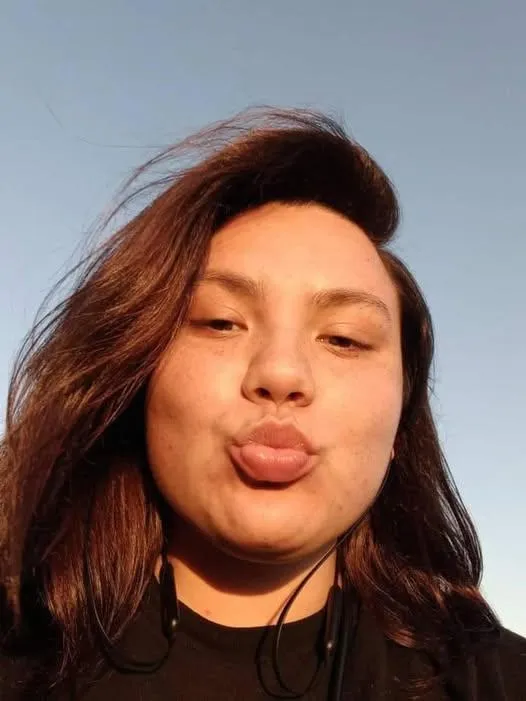 Kara Greger making a kissy face at the camera against a blue sky, her hair blowing