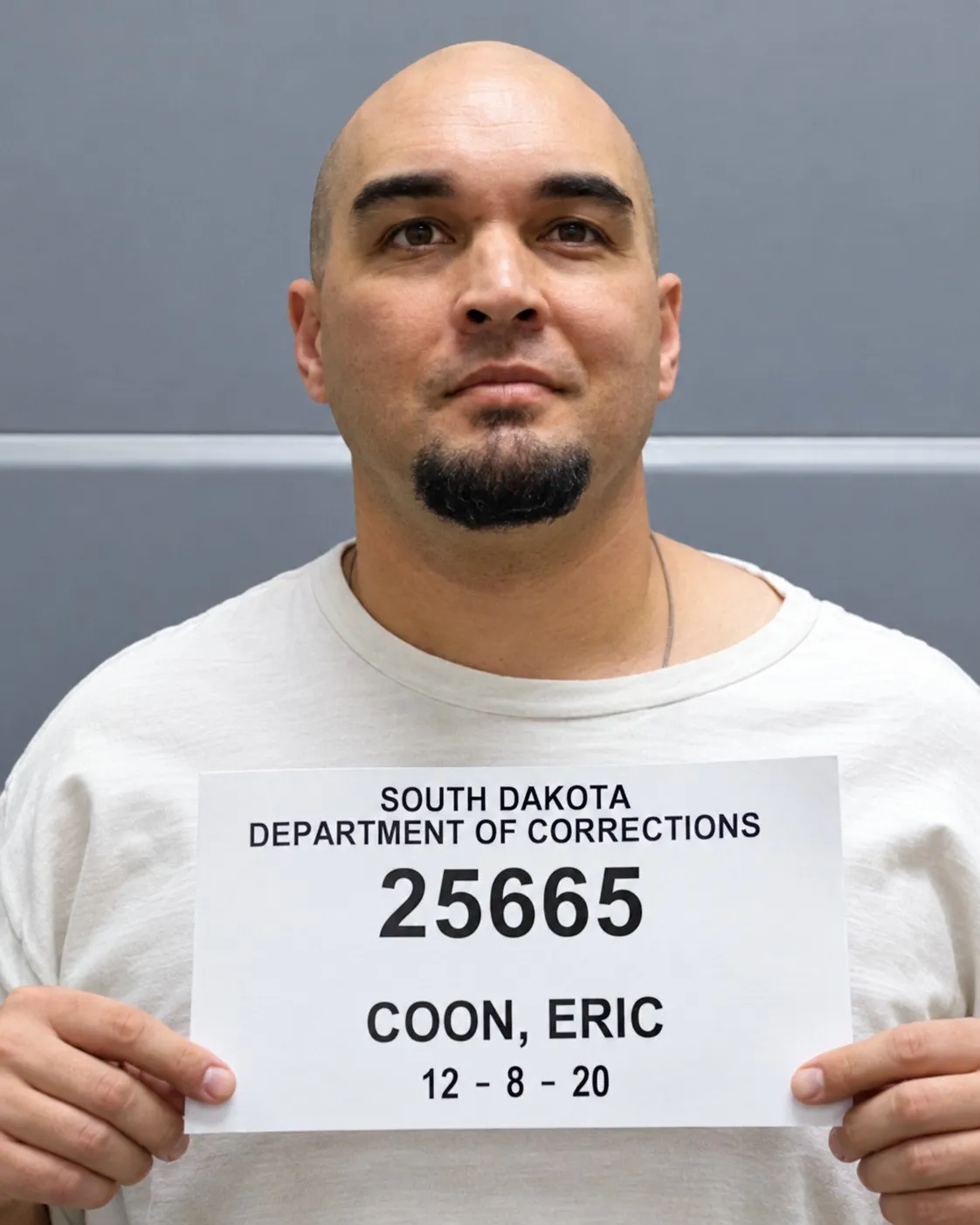 Eric Coon, older, with a shaved head and a goatee, holding a South Dakota Department of Corrections booking board