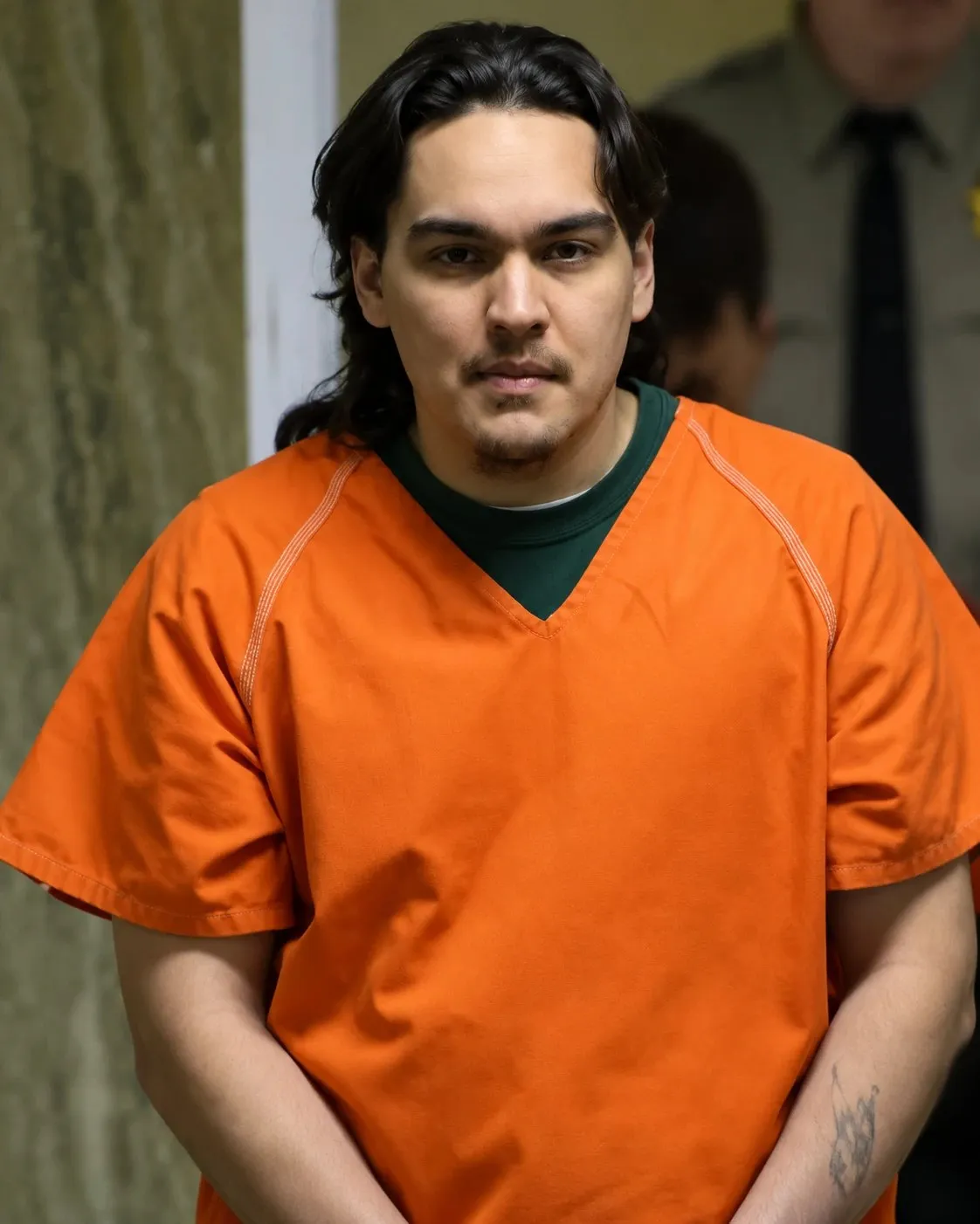 Eric Coon with long dark hair, in an orange jail uniform