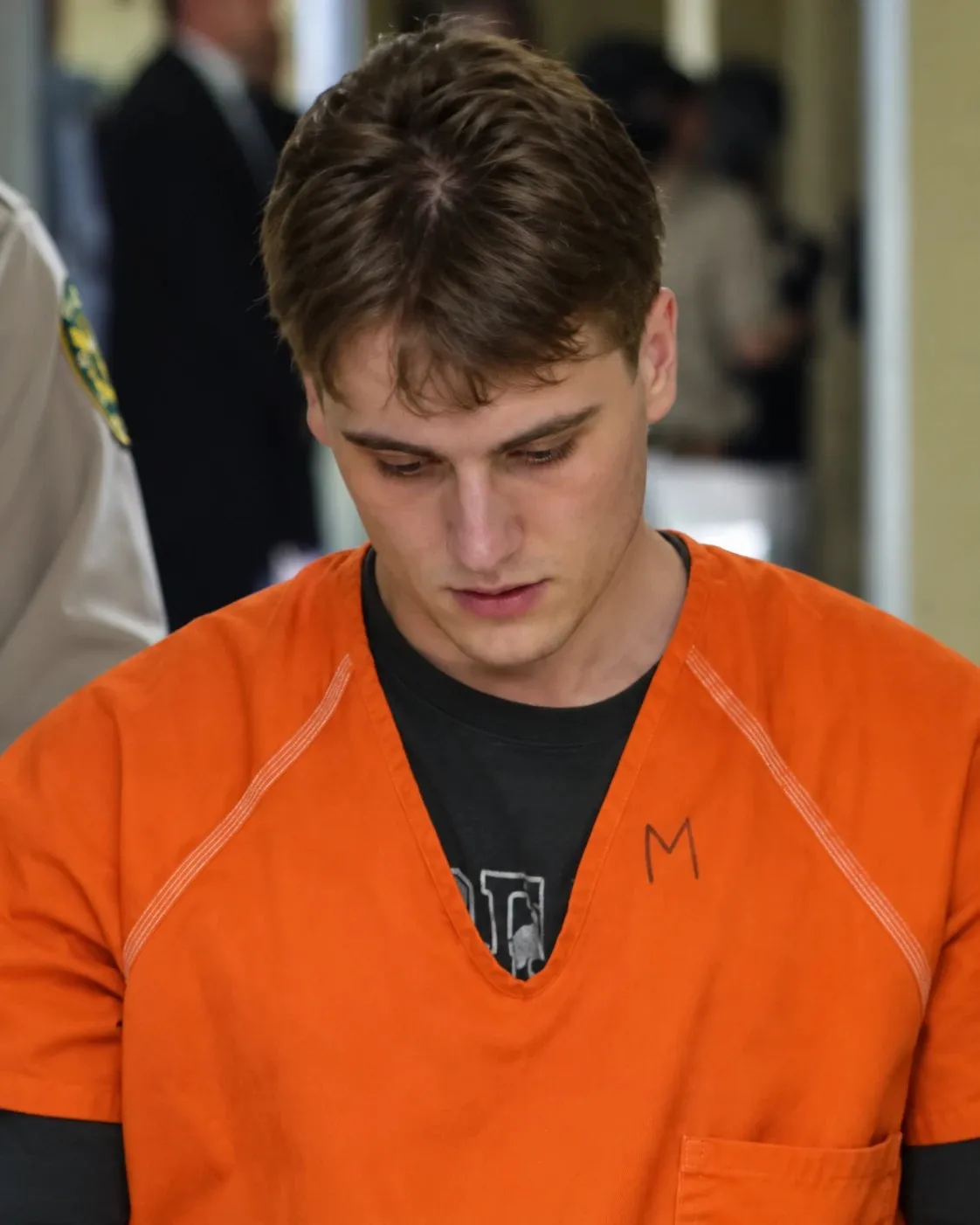 Robert Power, with short hair and an orange jail uniform, looking down
