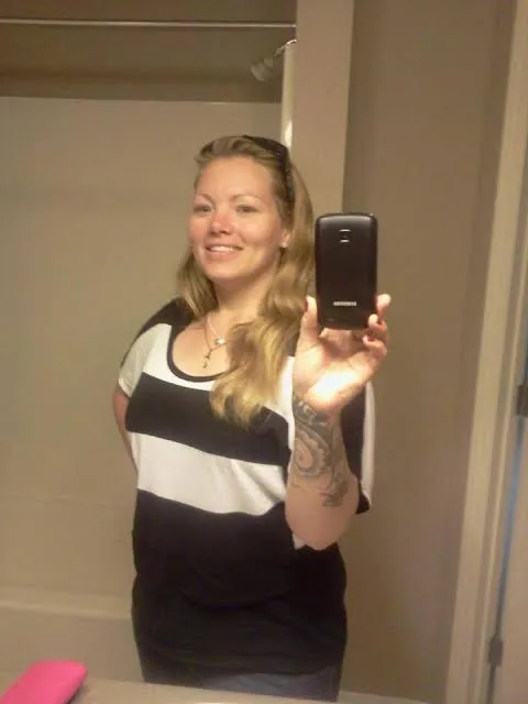 Rachel Cyriacks taking a mirror photo, her tattooed right forearm raised as she holds the phone