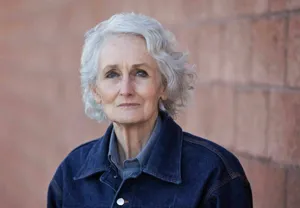 Margaret Rudin, with short gray hair, standing in front of a brick wall