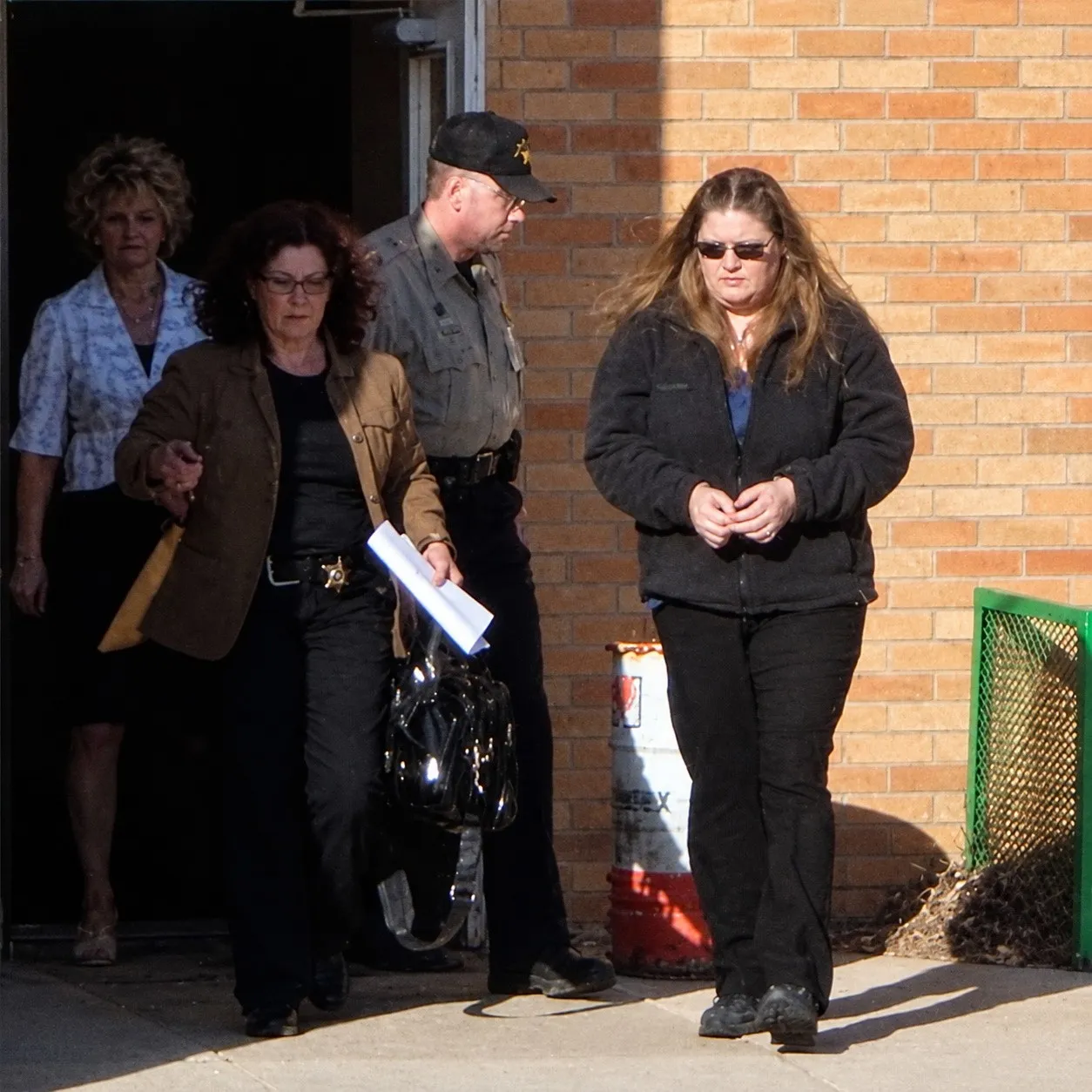 Four people walking out of a doorway in a brick building, among them a man in a sheriff’s uniform and cap
